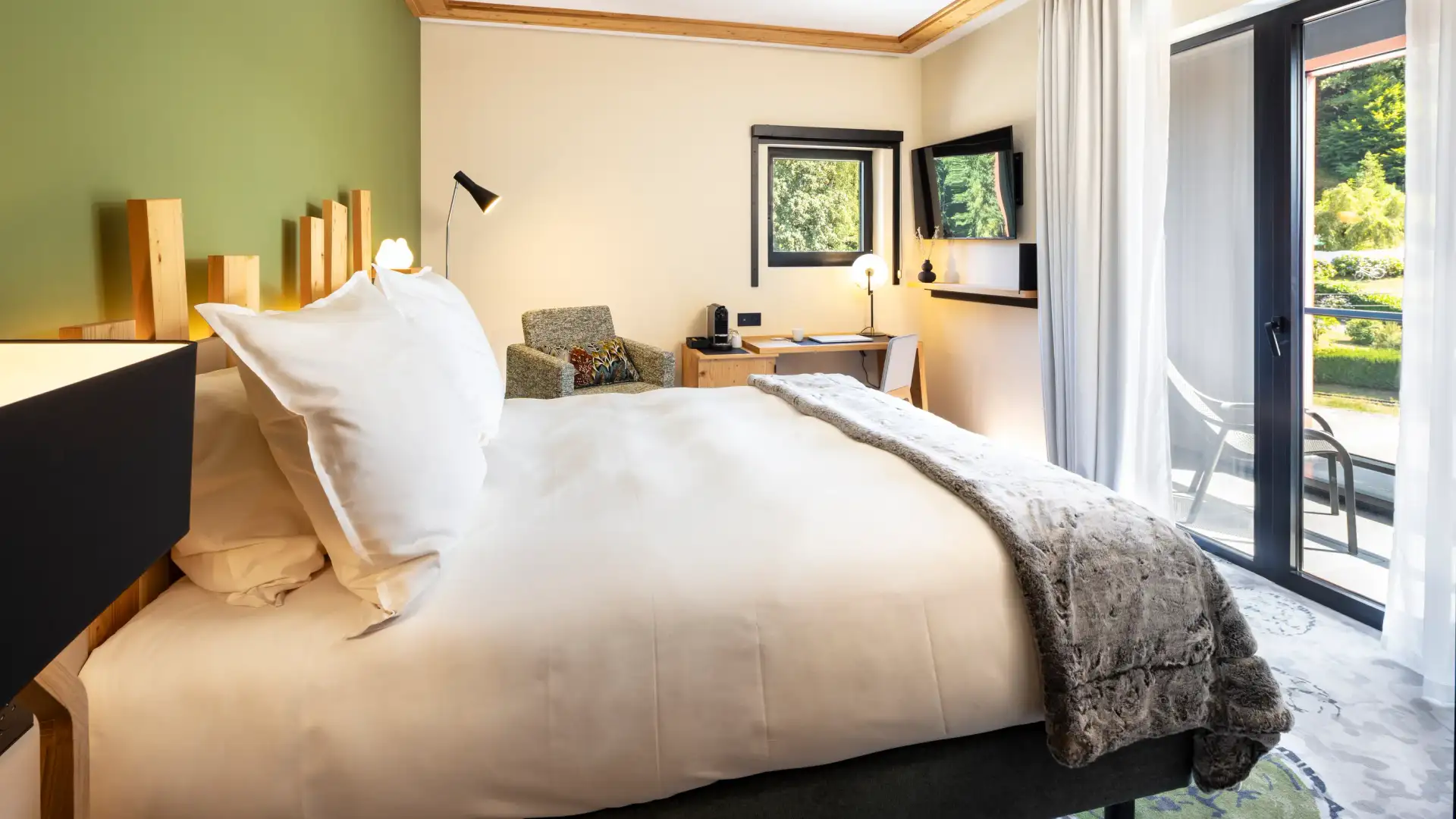 Room with a double bed, a bedside table, a desk, windows with an outside view, and a glass door leading to a balcony.