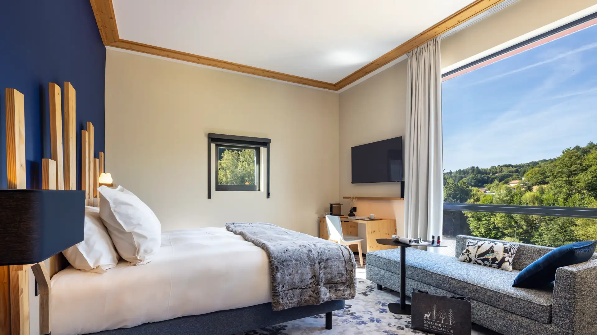 Zimmer mit einem Bett, einem Nachttisch, einem Sofa und einem großen Fenster mit Blick auf einen Wald