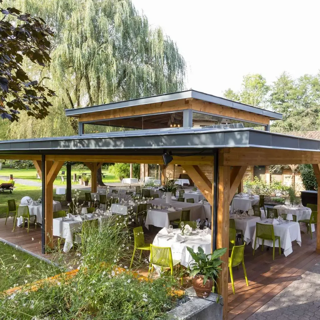 A covered wooden terrace with tables set for a meal, surrounded by trees and greenery.
