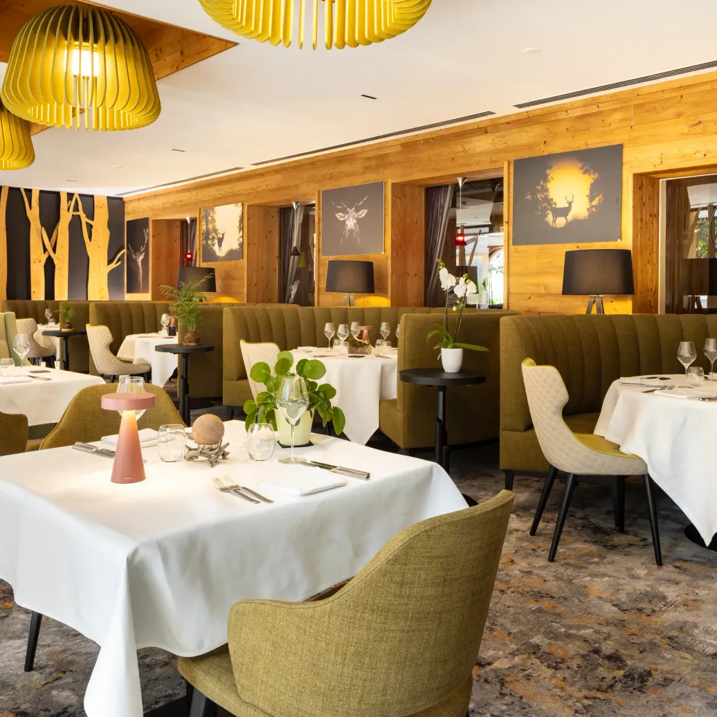 Elegant restaurant with set tables, green chairs, yellow lighting, and wooden walls