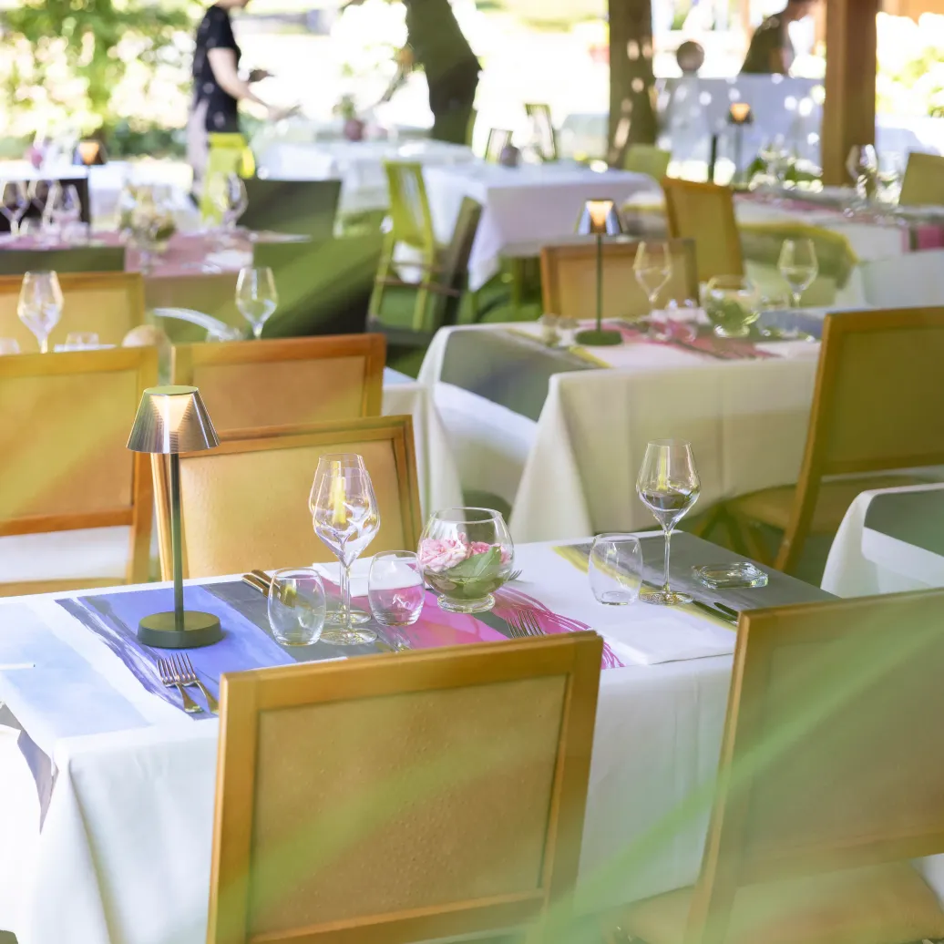 Tables dressées avec verres et bougies dans un cadre extérieur ombragé par des arbres