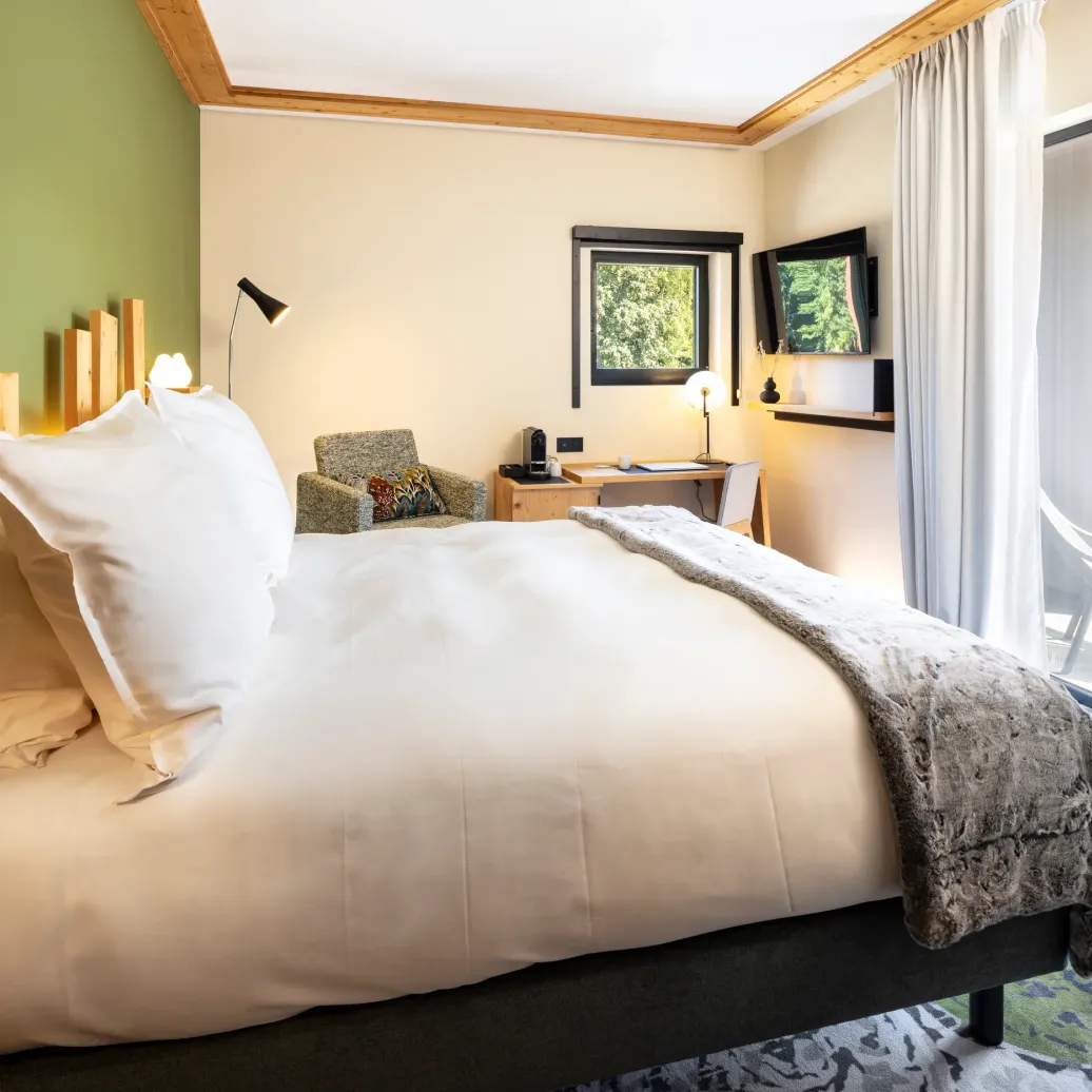 Room with a double bed, a bedside table, a desk, windows with an outside view, and a glass door leading to a balcony.