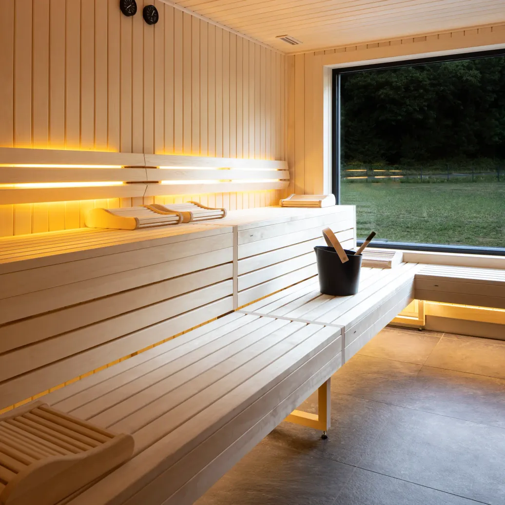 Wooden sauna room with benches, a window overlooking an outdoor view, and a bucket with accessories