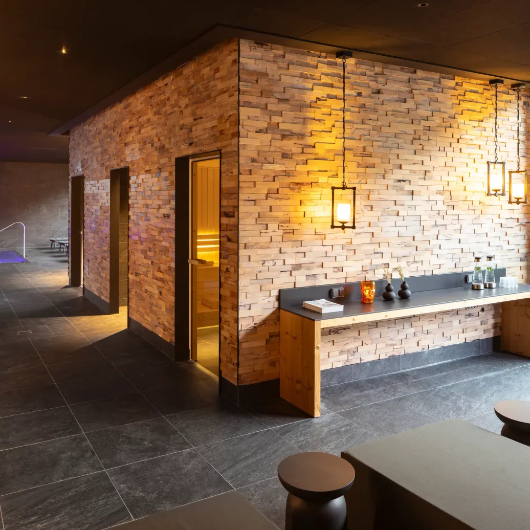 Modern interior with a lit brick wall, a wooden counter, and open doors leading to a dimly lit room