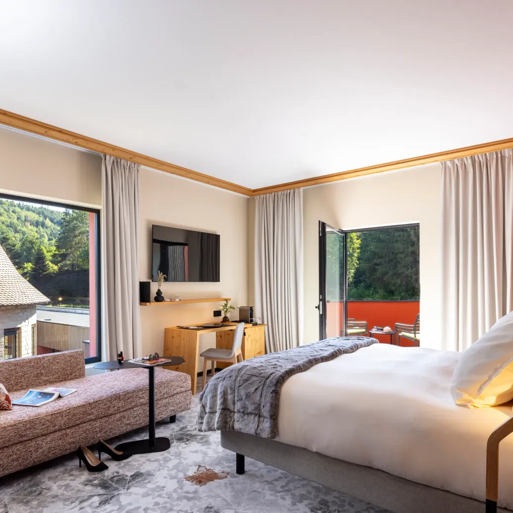 Bright room with bed, sofa, desk and view of traditional rooftops and a forest
