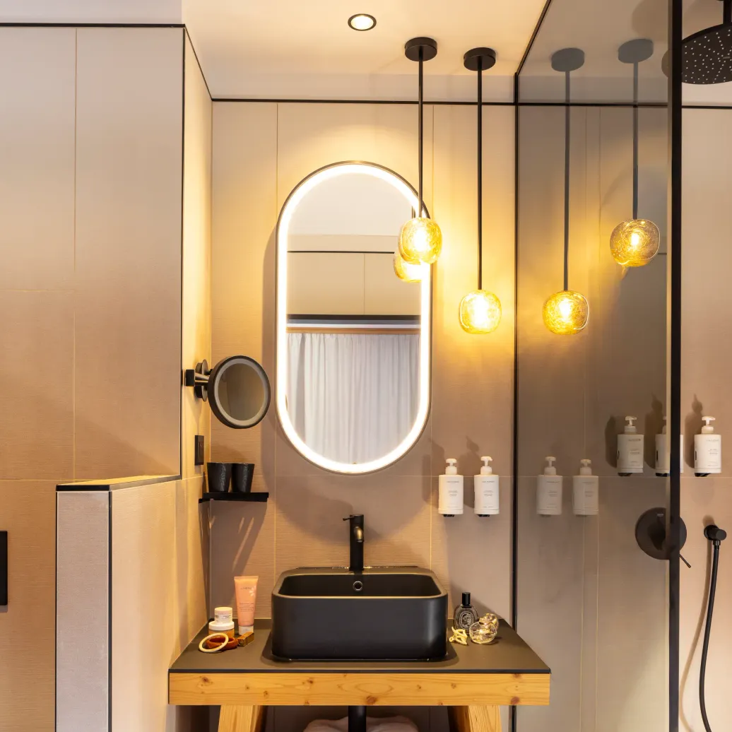 Modern bathroom with black sink, oval mirror, and rain shower effect