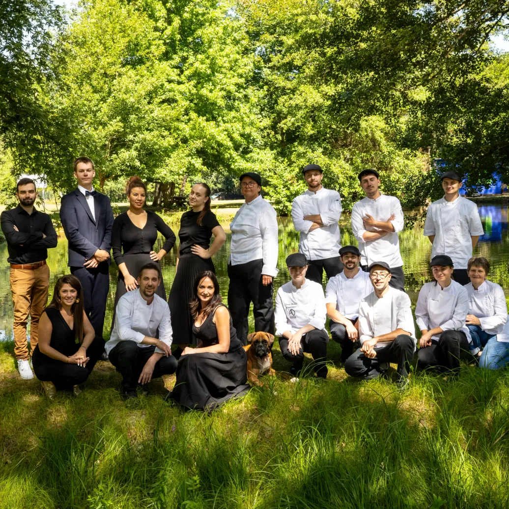 A group of people in professional attire poses in front of a body of water surrounded by trees.