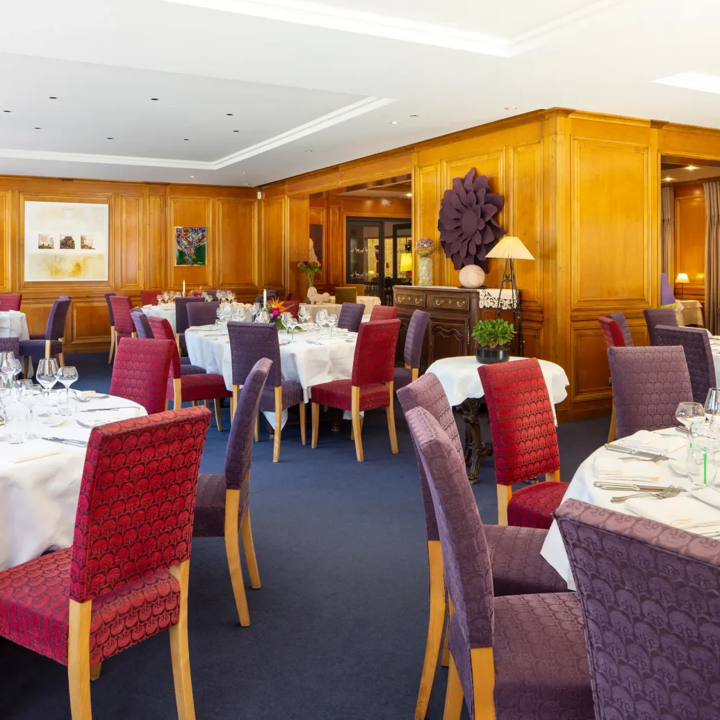 Elegant restaurant room with set tables, white tablecloths, padded chairs, and floral decor