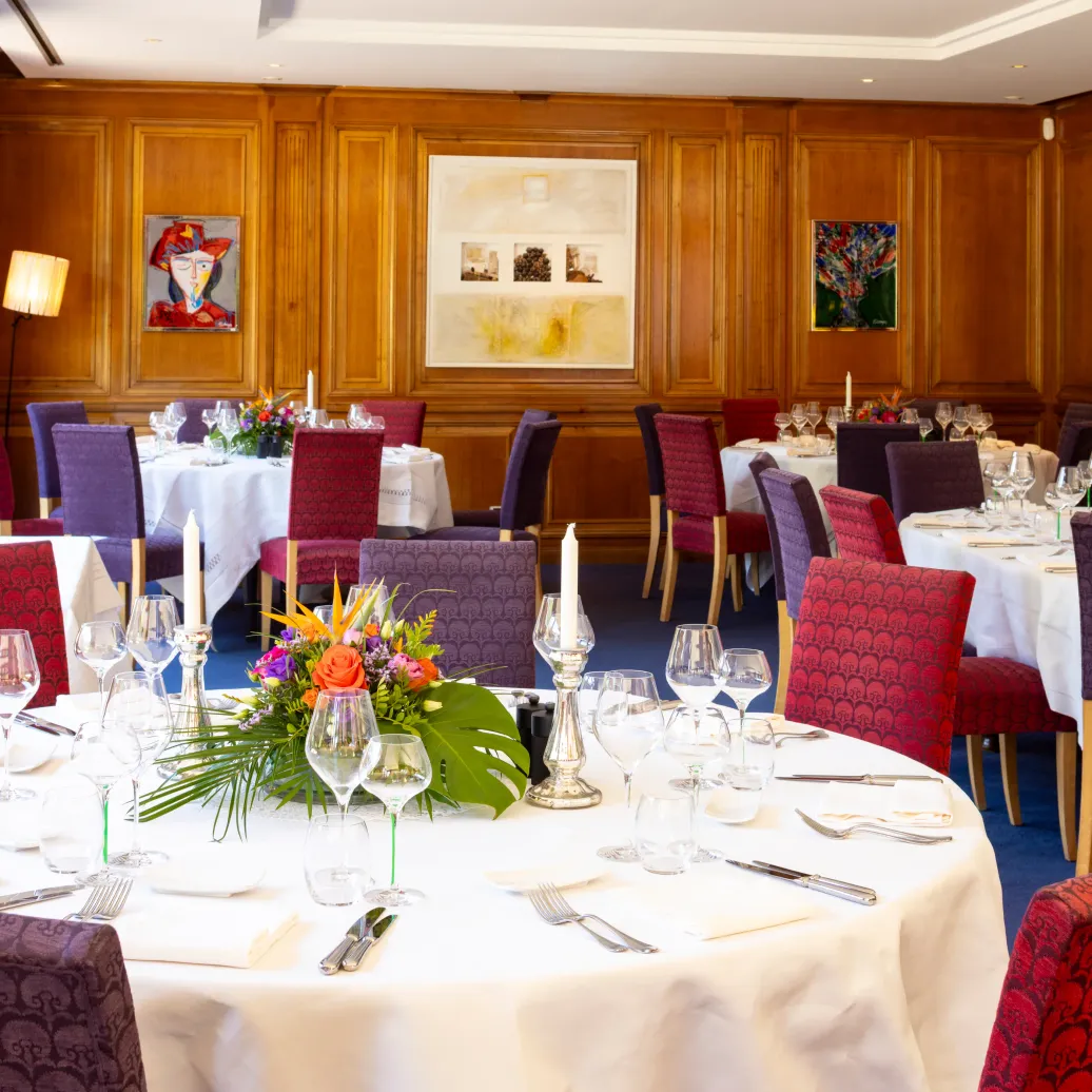 An elegant dining room with set tables, candelabras, glasses, and flowers at the center of the tables.