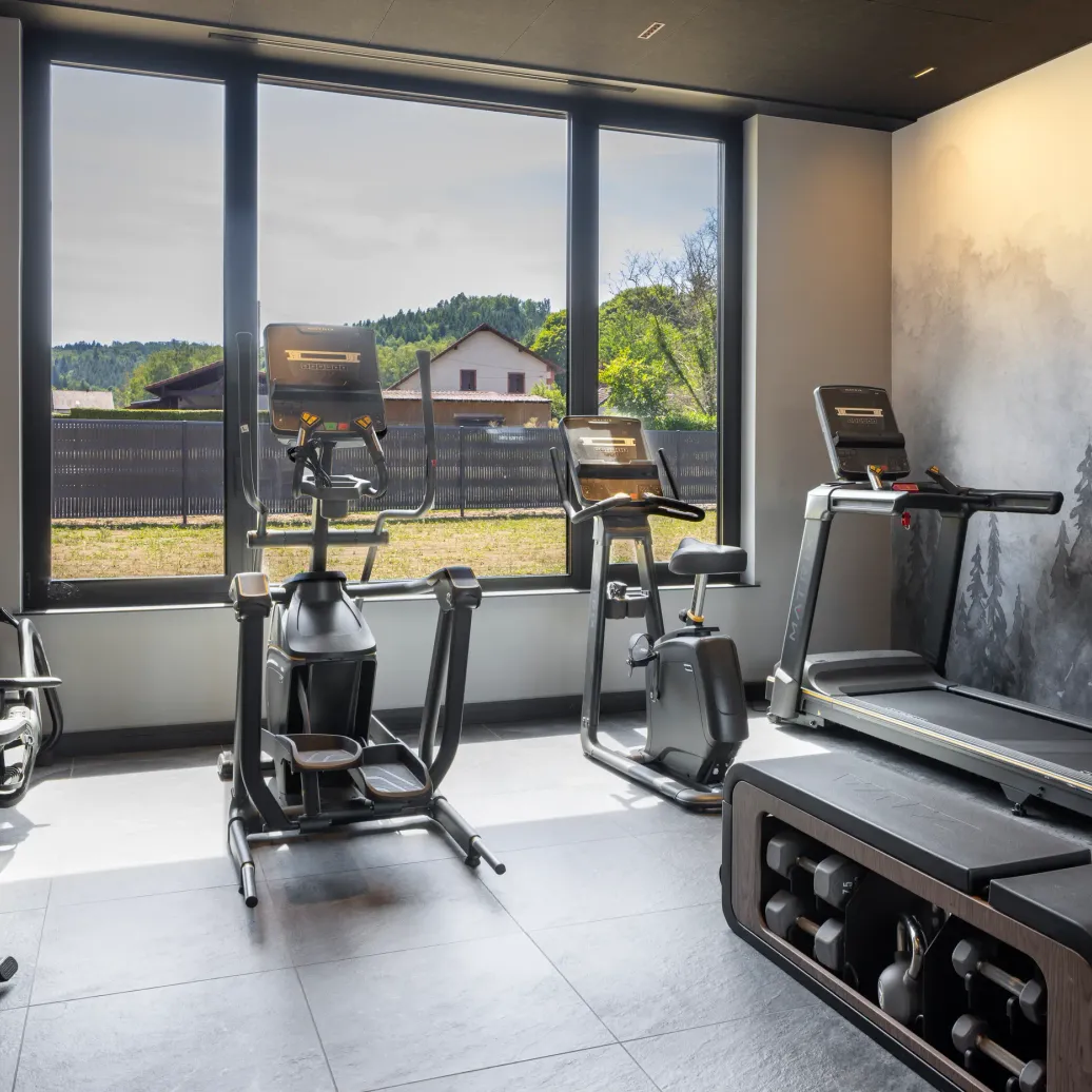 Gym with several fitness machines in front of large windows overlooking an outdoor view