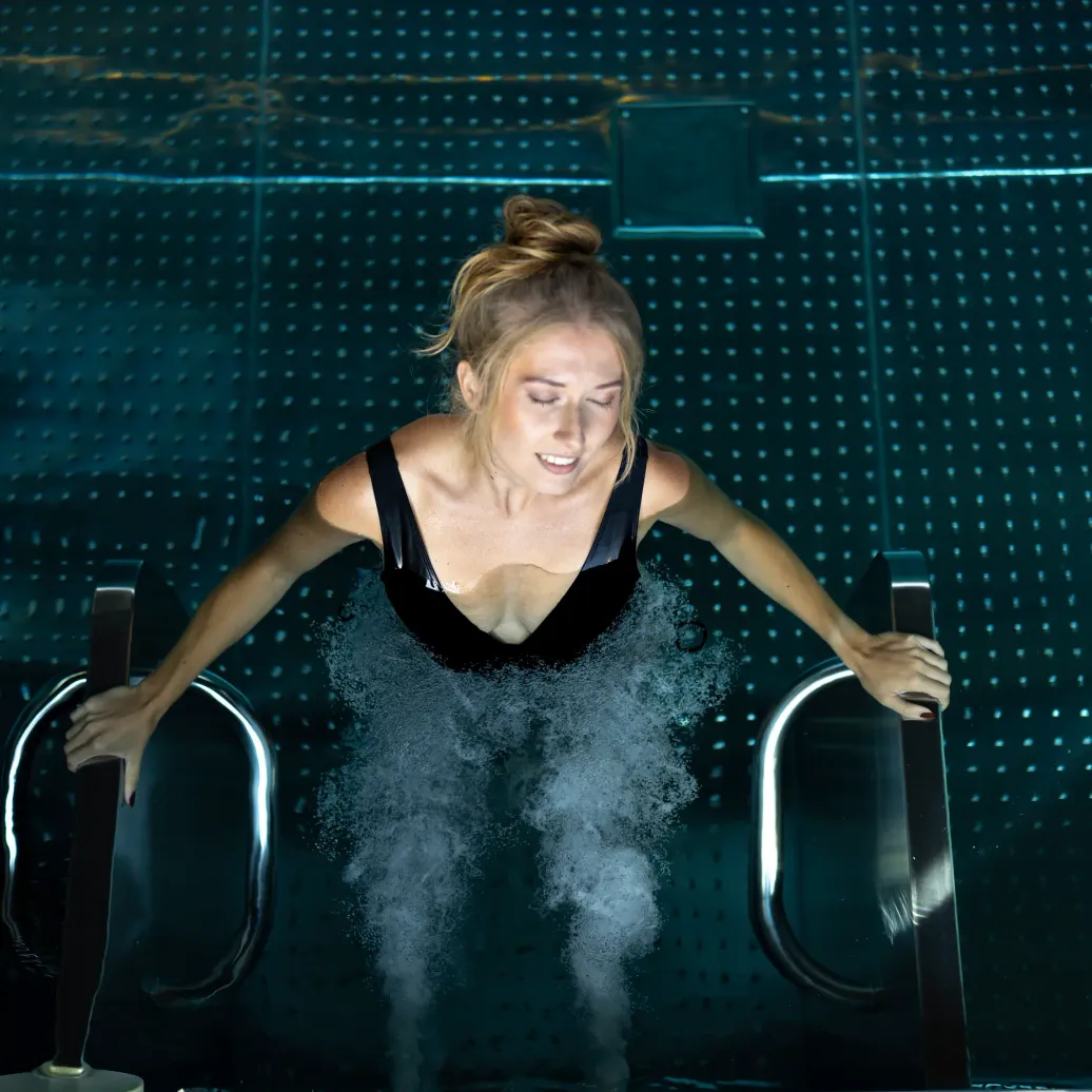 A woman in sportswear exercises in a pool with visible water jets around her.