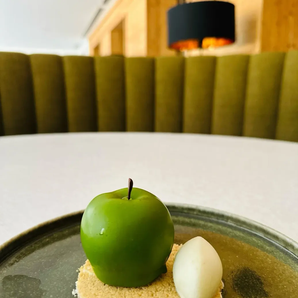 A dessert made of a green apple and a white ice cream ball on a crumble base, served on a green plate