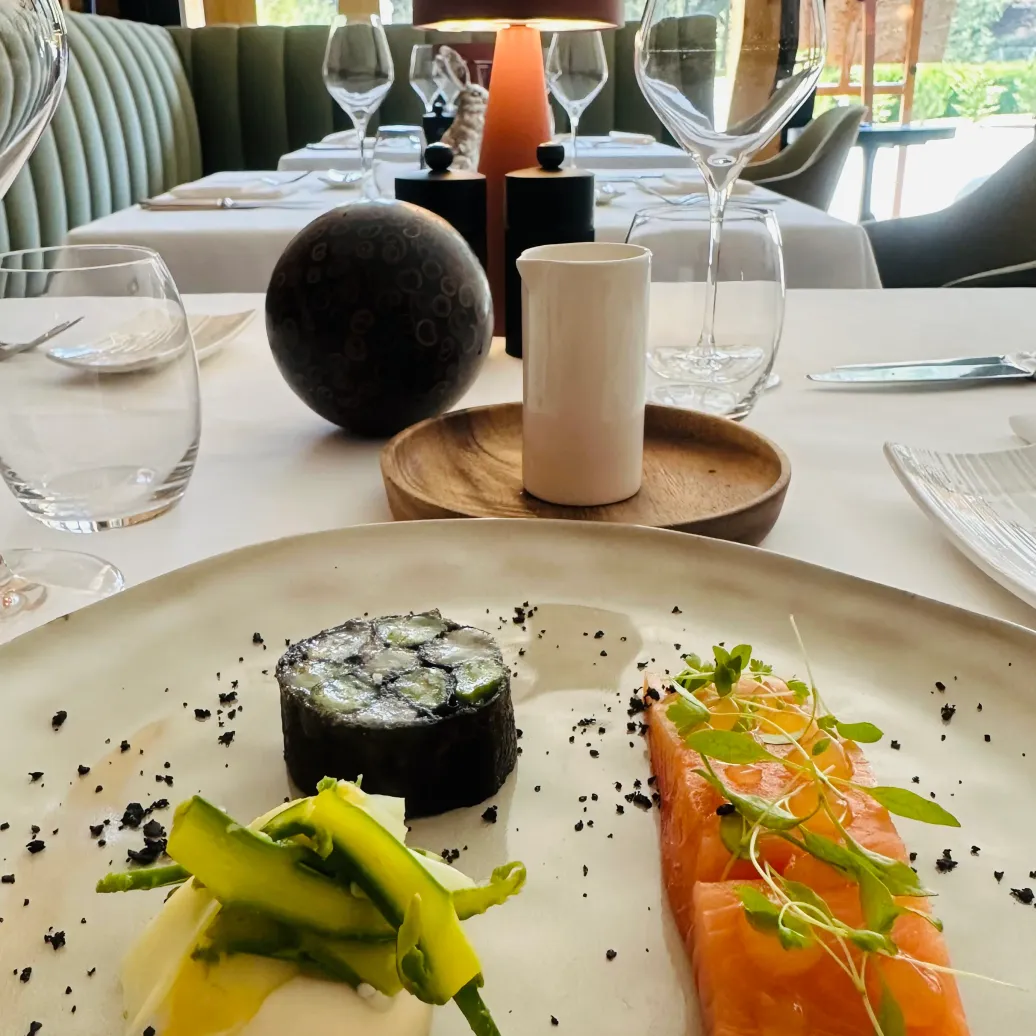 Plate of fine dishes with sushi, salmon, and vegetables, placed on an elegant table with wine glasses and decoration.