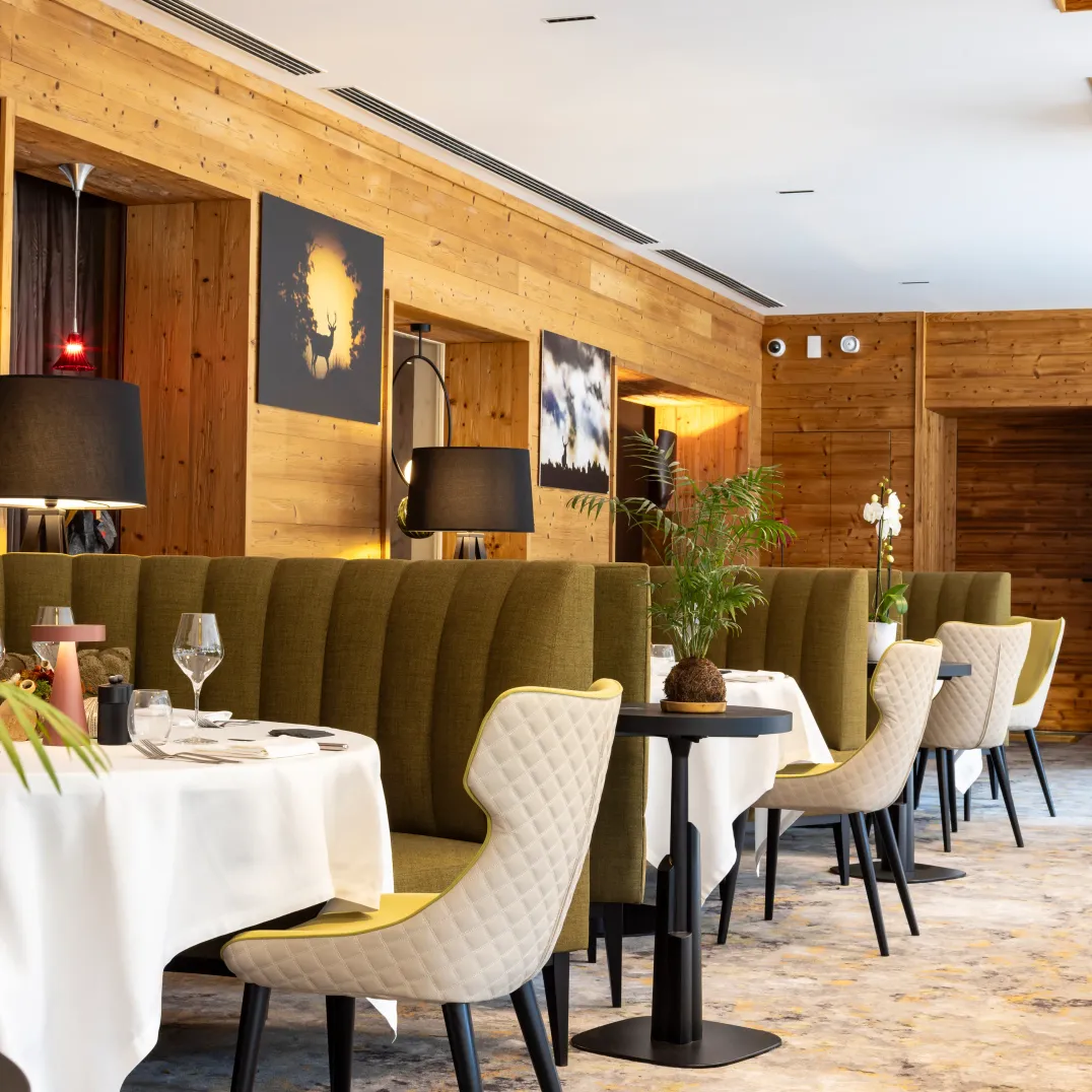 Restaurant mit Tischen und Stühlen entlang einer Holzwand, Pflanzen und Lampen auf den Tischen