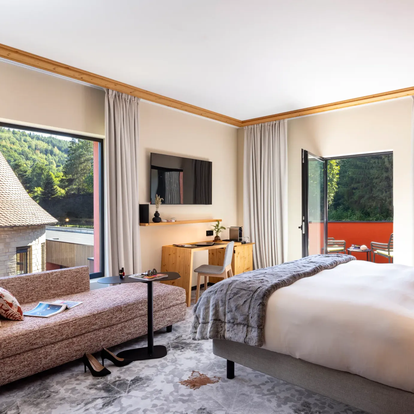 Room with bed, sofa, desk and view of traditional rooftops and a forest