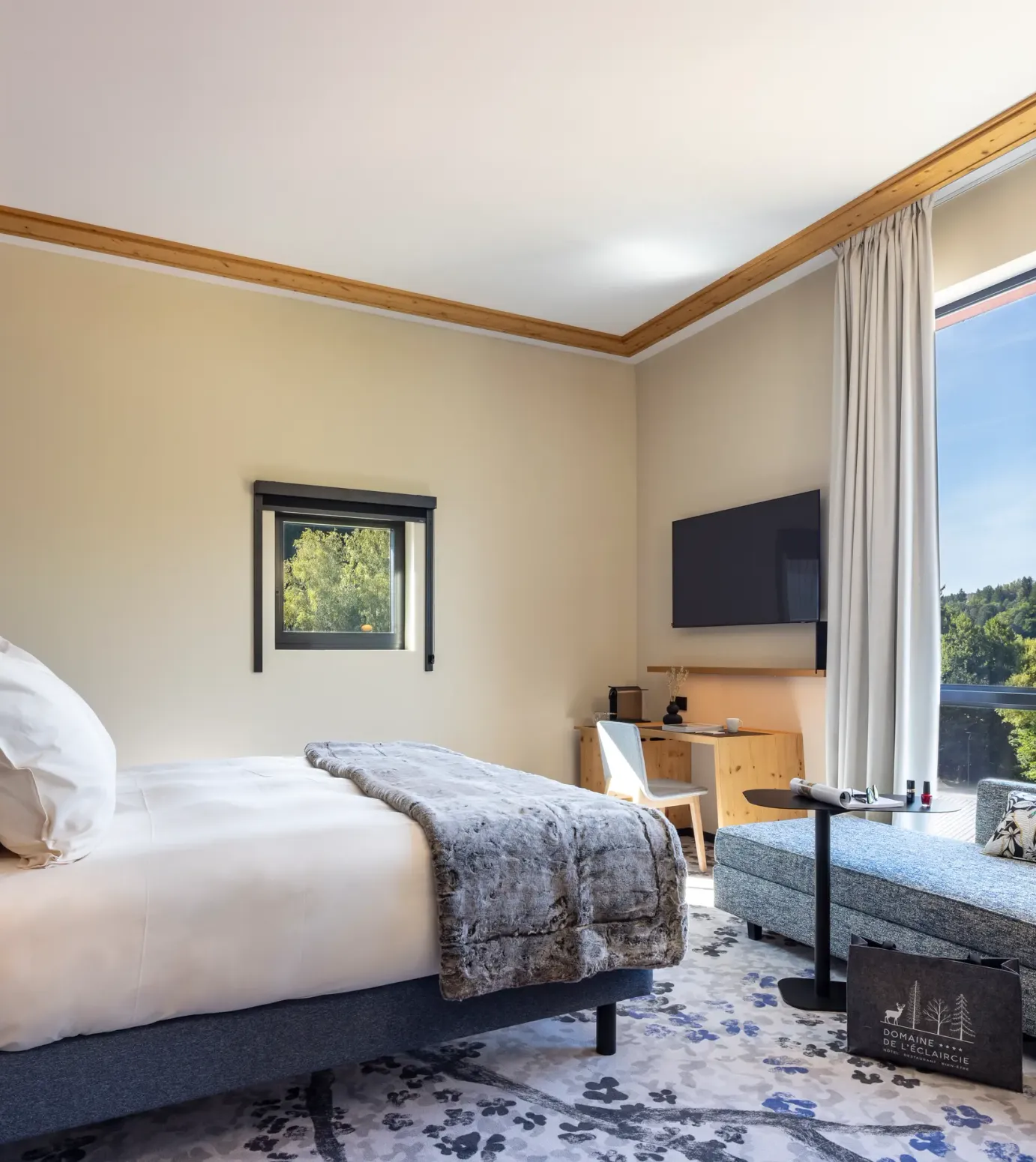 Zimmer mit einem Bett, einem Nachttisch, einem Sofa und einem großen Fenster mit Blick auf einen Wald