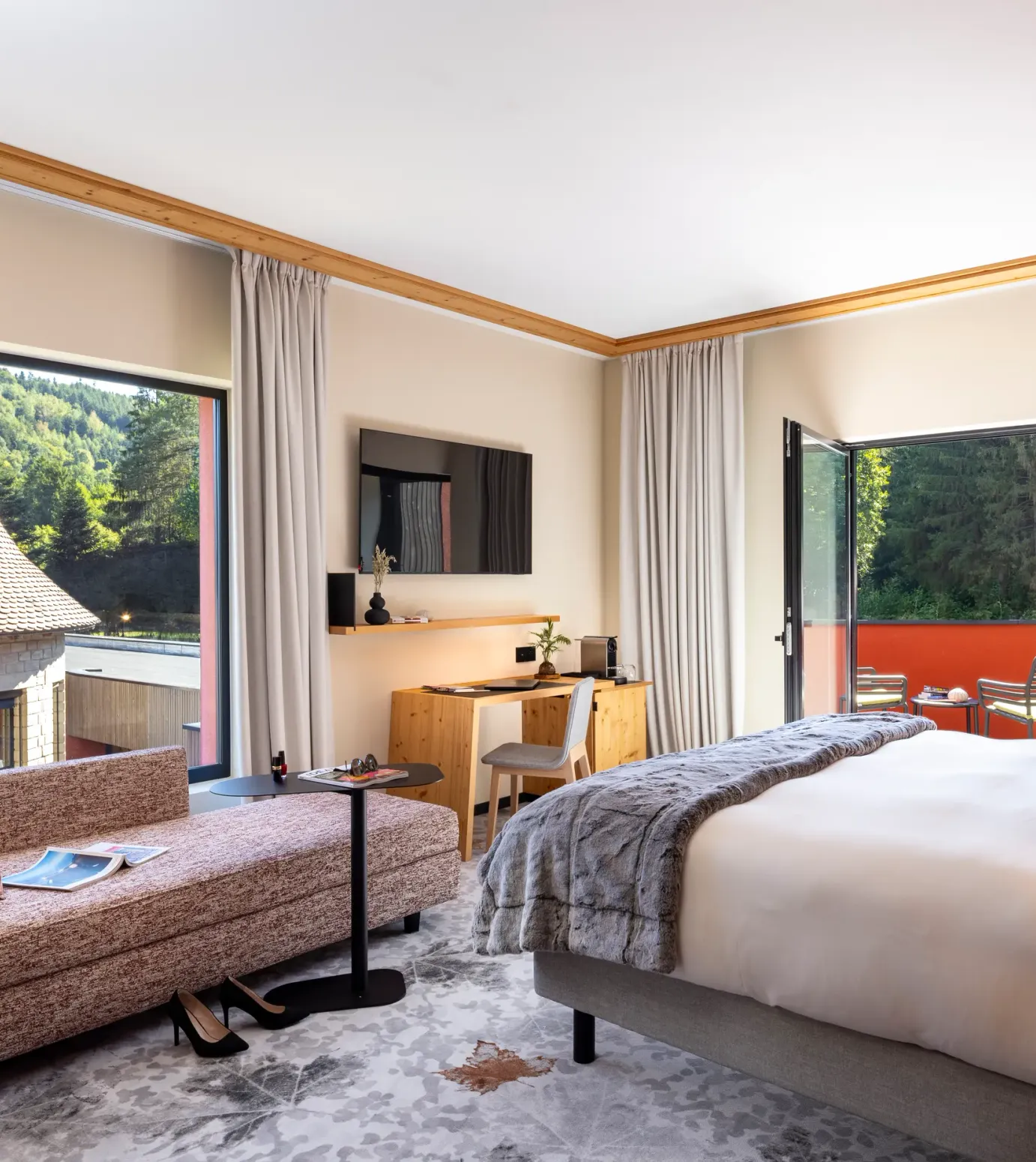Zimmer mit Bett, Sofa, Schreibtisch und Blick auf traditionelle Dächer und einen Wald