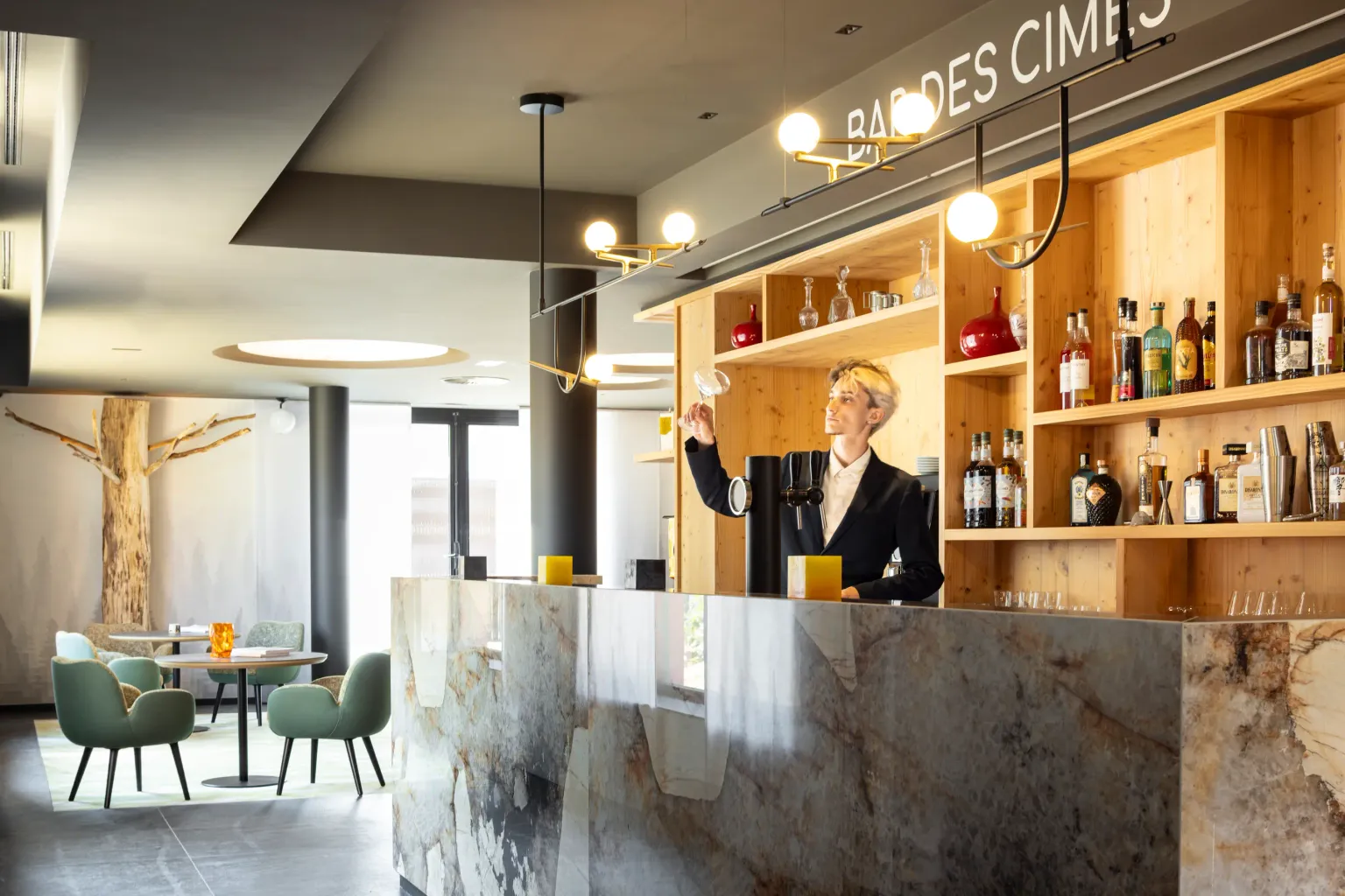 A bartender prepares a drink behind a marble counter, with wooden shelves filled with bottles behind him.