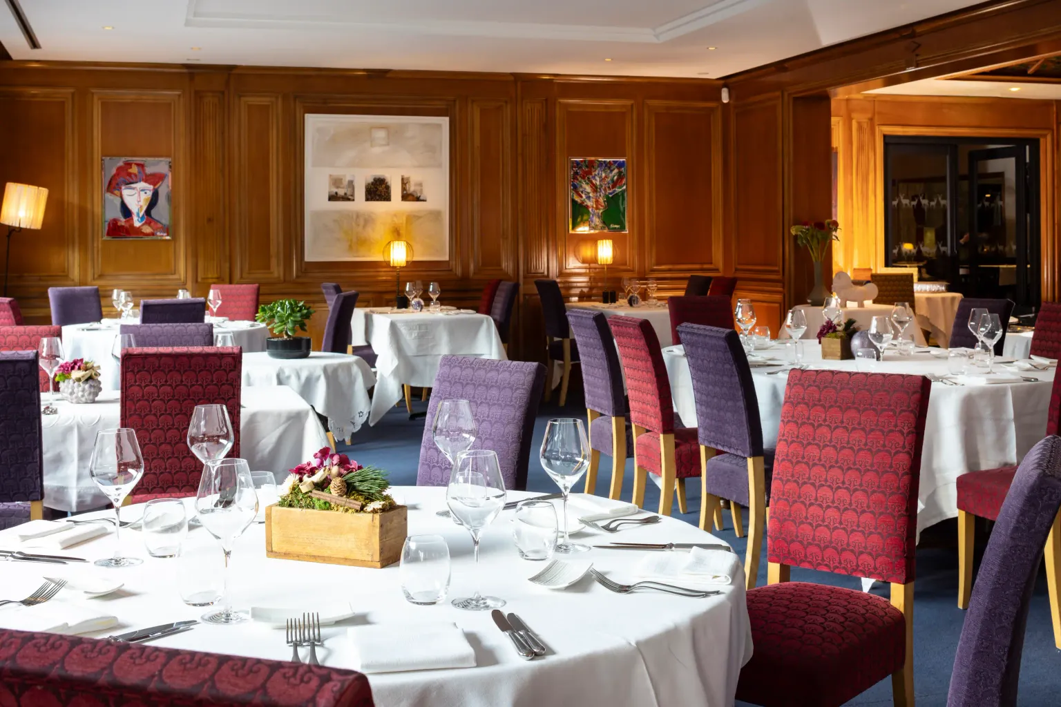 Elegant restaurant room with set tables, padded chairs, and artwork on the walls