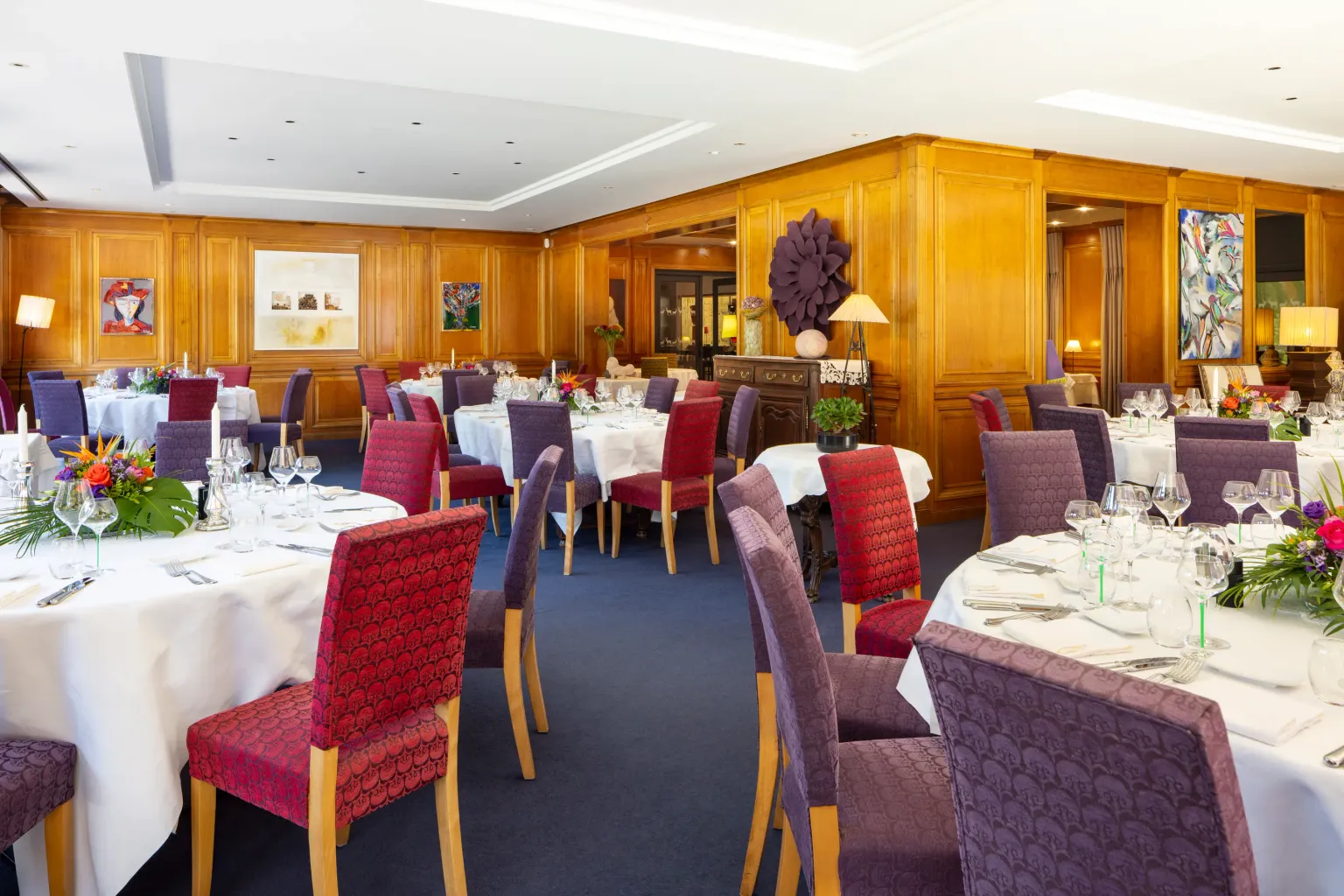 Salle de restaurant élégante avec tables dressées, nappes blanches, chaises rembourrées et décor floral