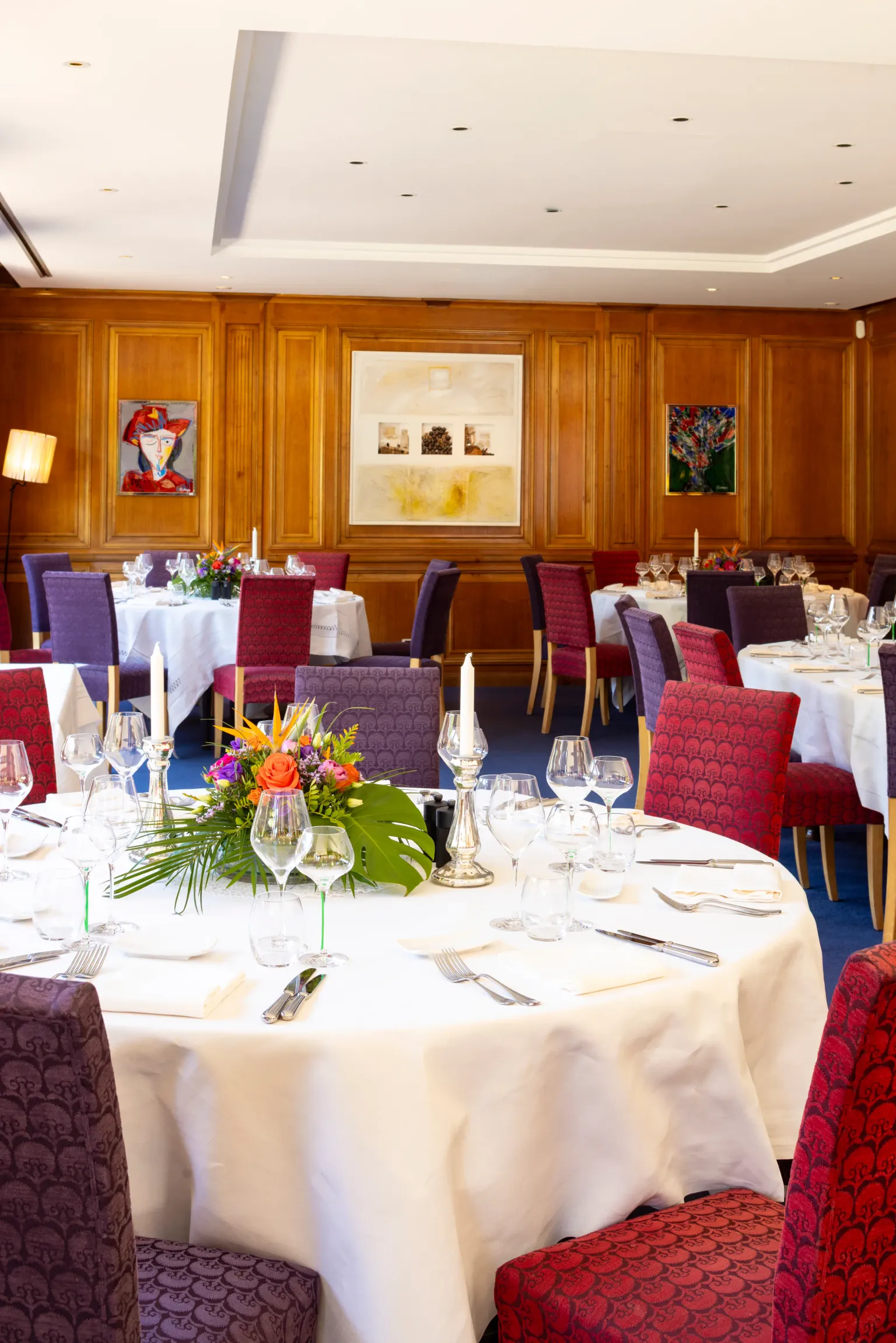 An elegant dining room with set tables, candelabras, glasses, and flowers at the center of the tables.