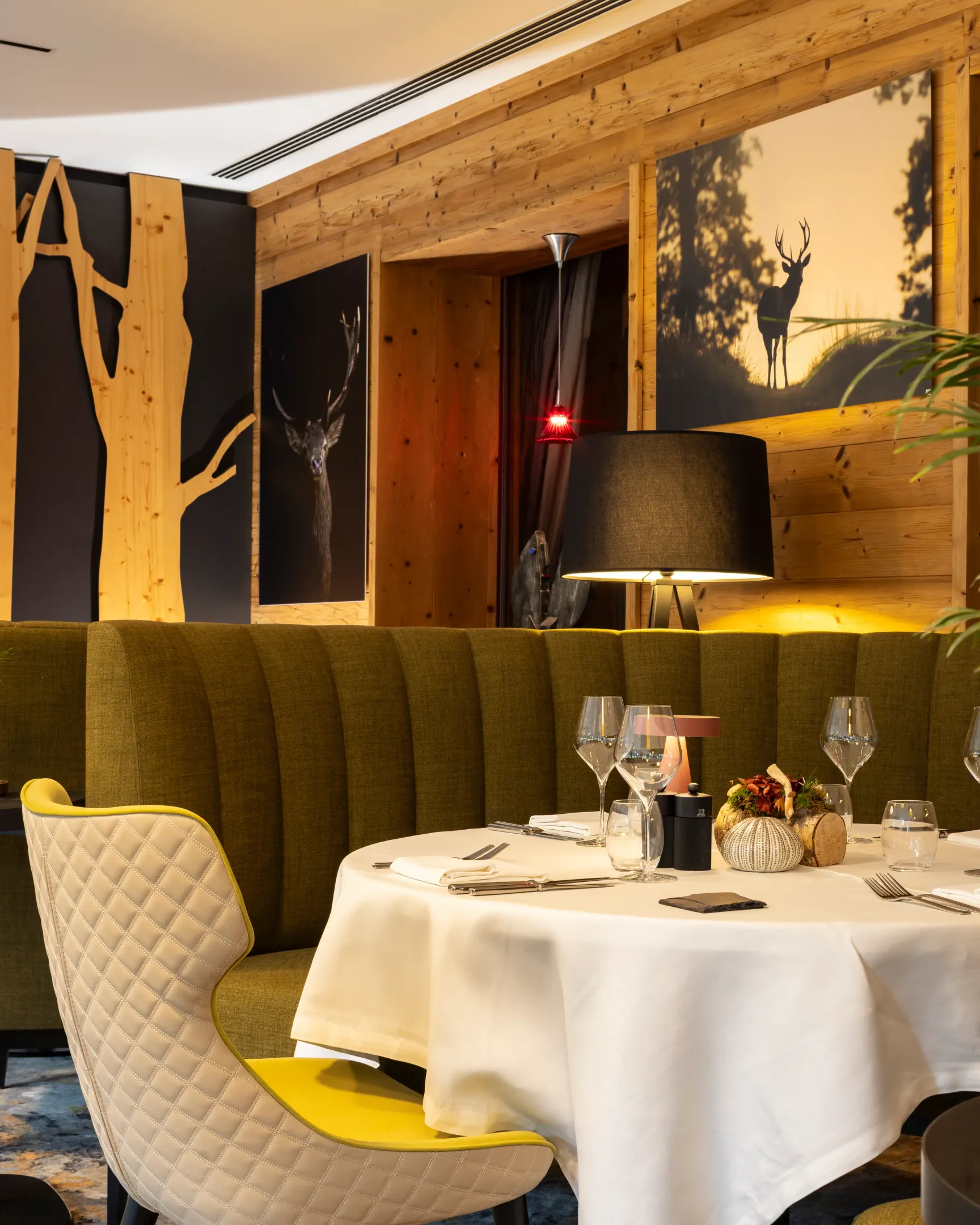 Table set with glasses and cutlery in a restaurant with wooden and green decor, featuring candelabras and wall art.