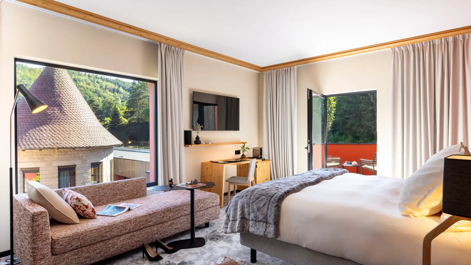 Chambre avec lit, canapé, bureau et vue sur des toits traditionnels et une forêt
