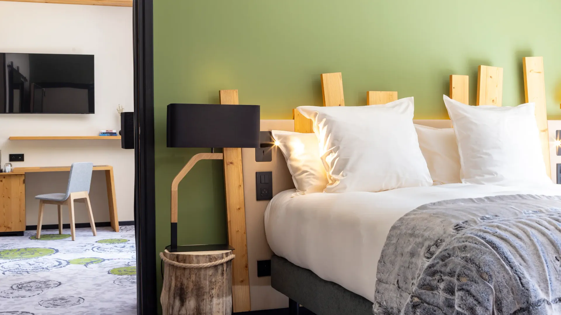 Hotelzimmer mit einem Doppelbett, einer Holz-Nachttischlampe, einem Fernseher und einem Schreibtisch mit einem Stuhl