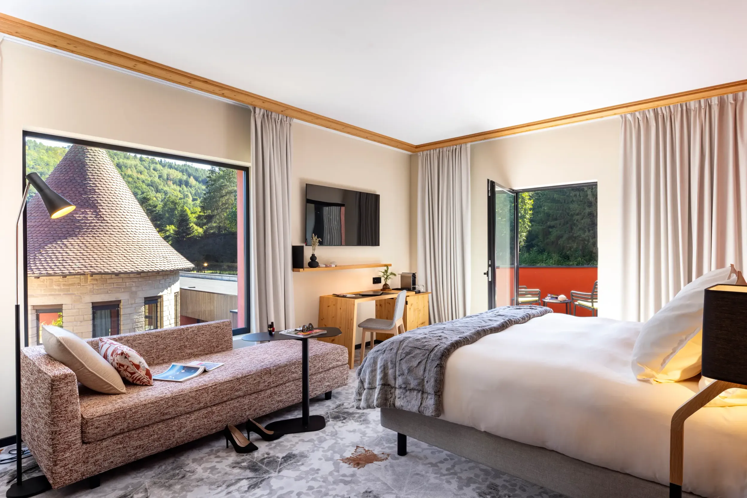 Chambre avec lit, canapé, bureau et vue sur des toits traditionnels et une forêt