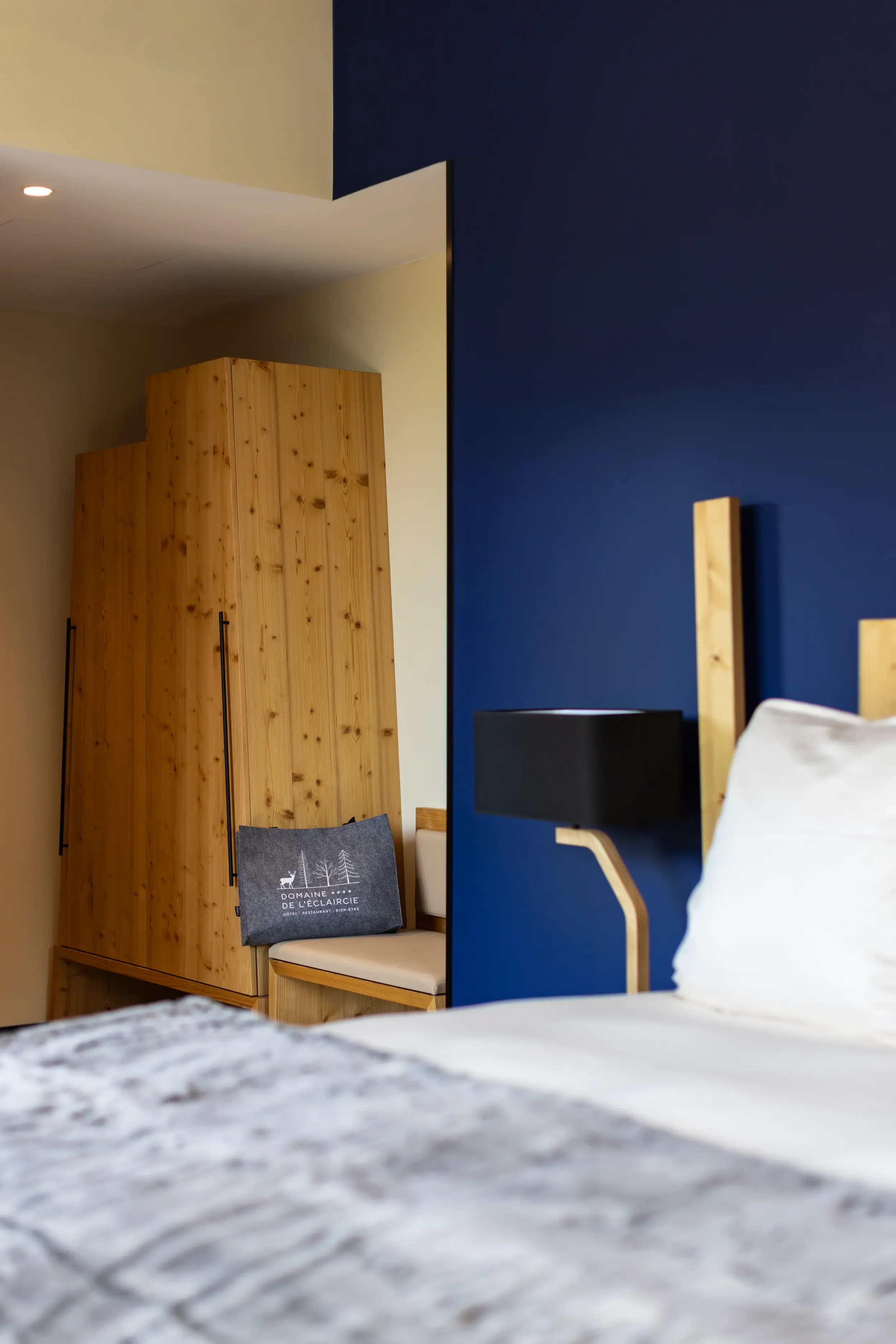 Zimmer mit Bett, hölzernem Kopfteil, blau und beige gestrichenen Wänden und Kissen mit Text und Logo