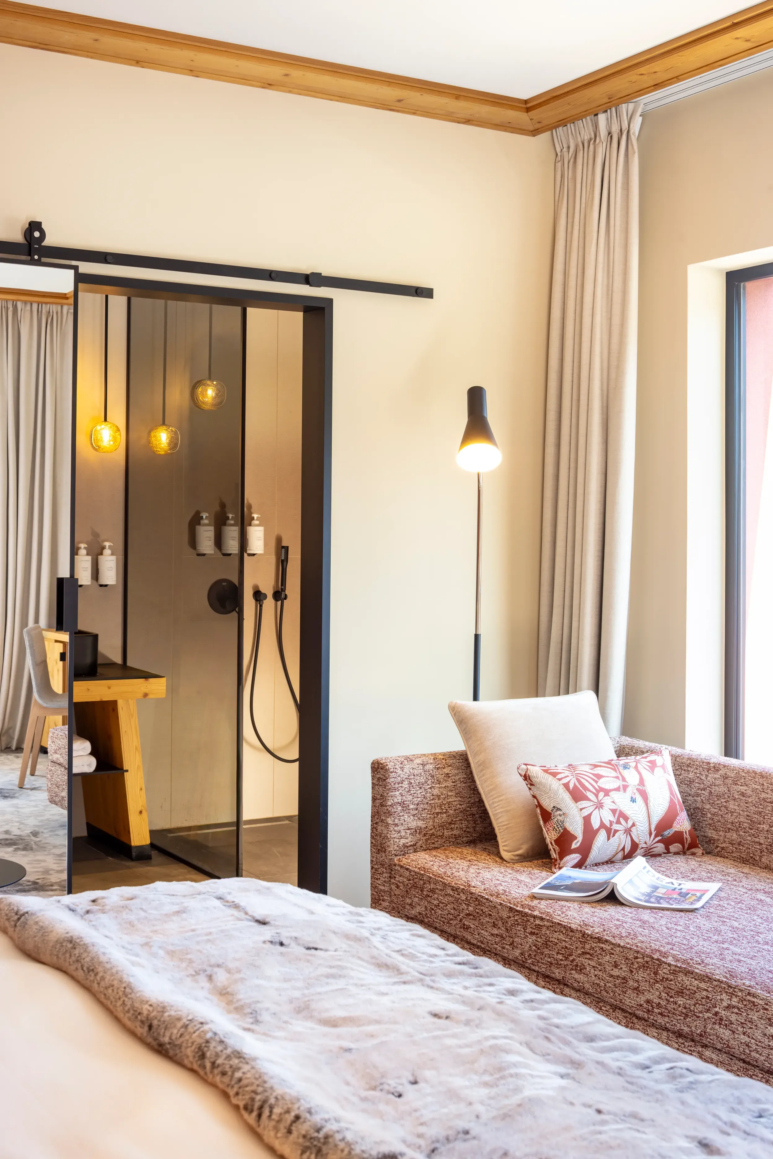 Chambre avec lit recouvert d'une couverture blanche, canapé avec coussins, table de chevet et porte de douche ouverte éclairée