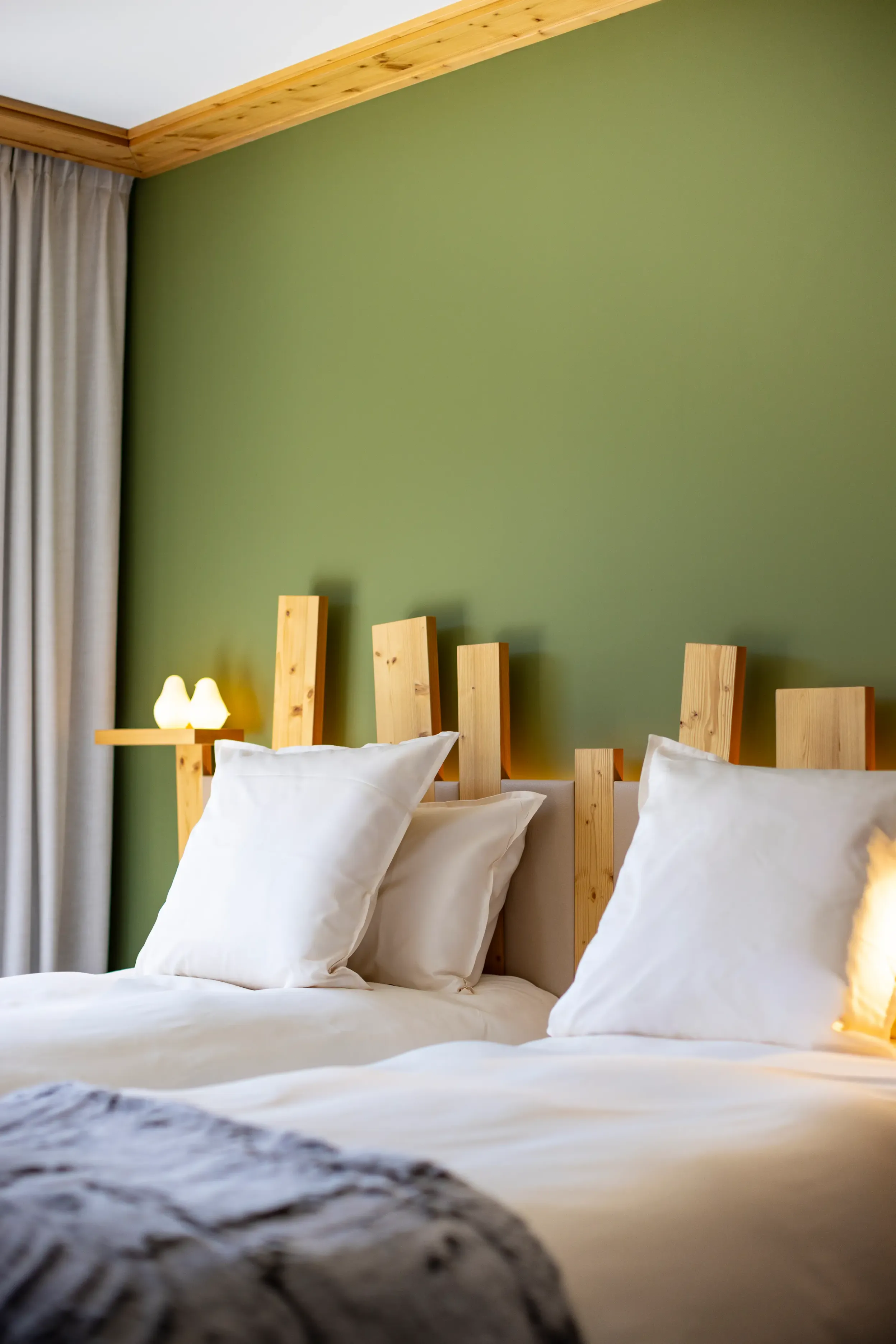 Bett mit Holz-Kopfteil und weißen Kissen in einem Zimmer mit grünen Wandmalereien
