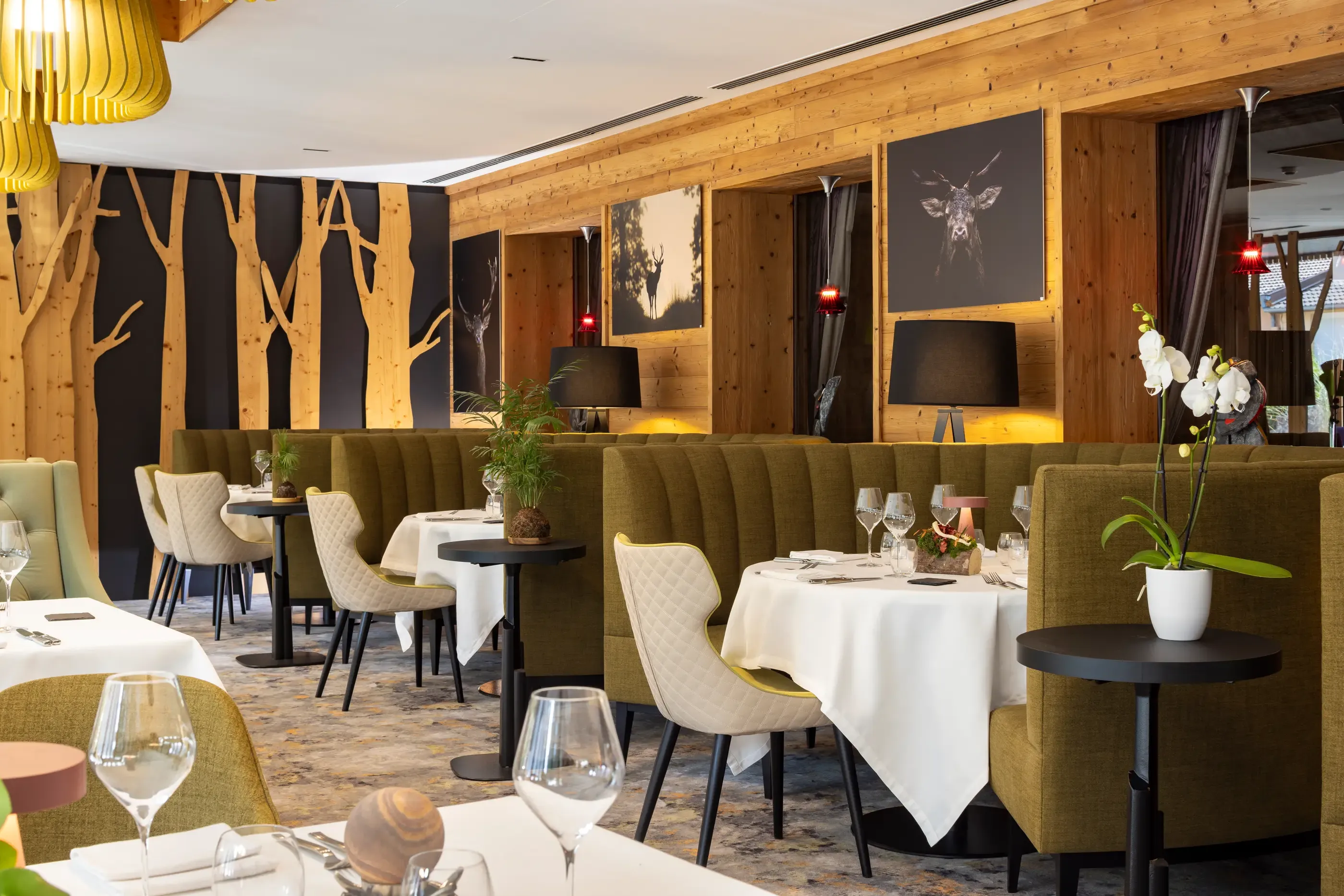 Elegant restaurant with set tables, green banquettes, and wooden walls decorated with animal photos.