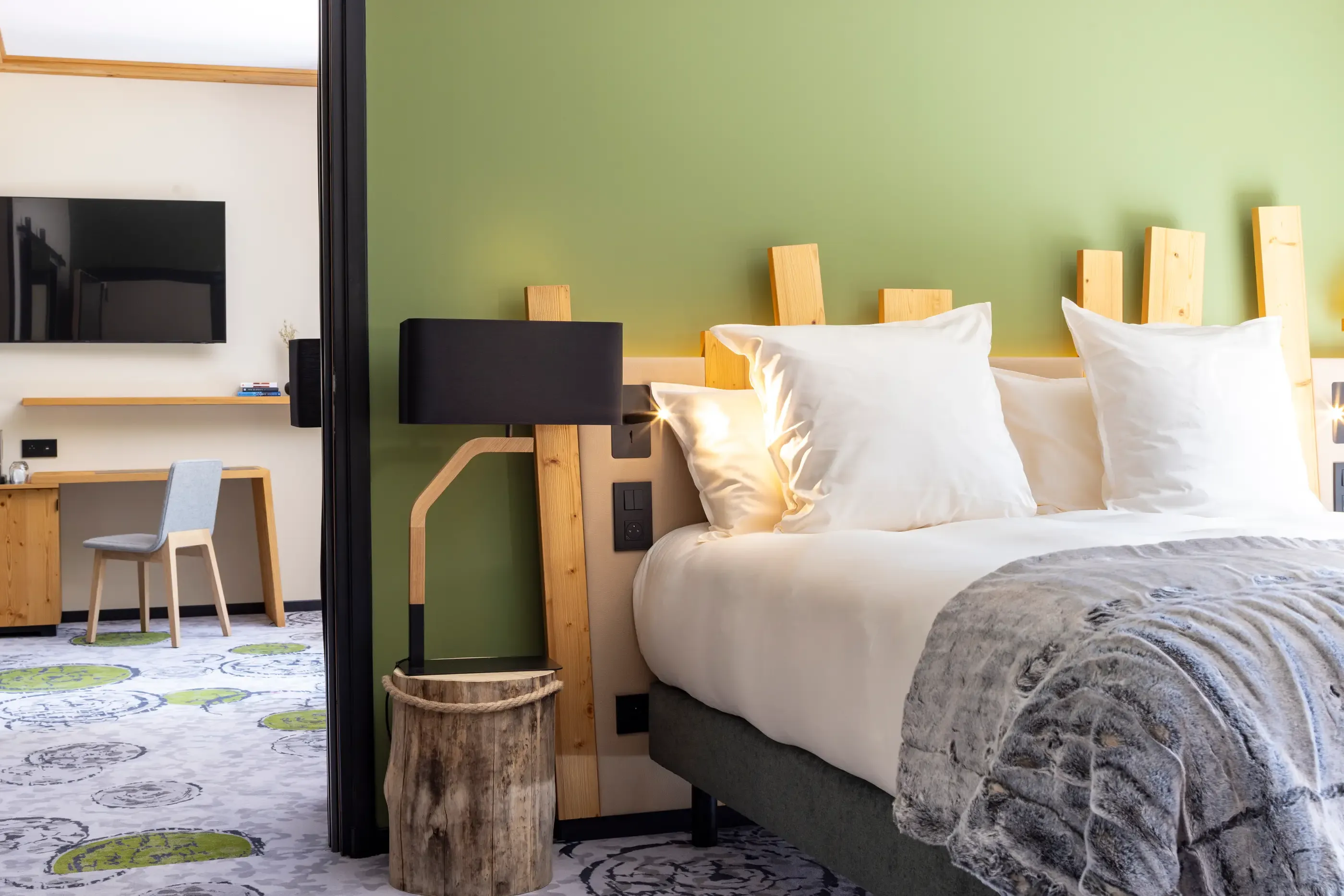 Hotel room with a double bed, a wooden bedside lamp, a television, and a desk with a chair.
