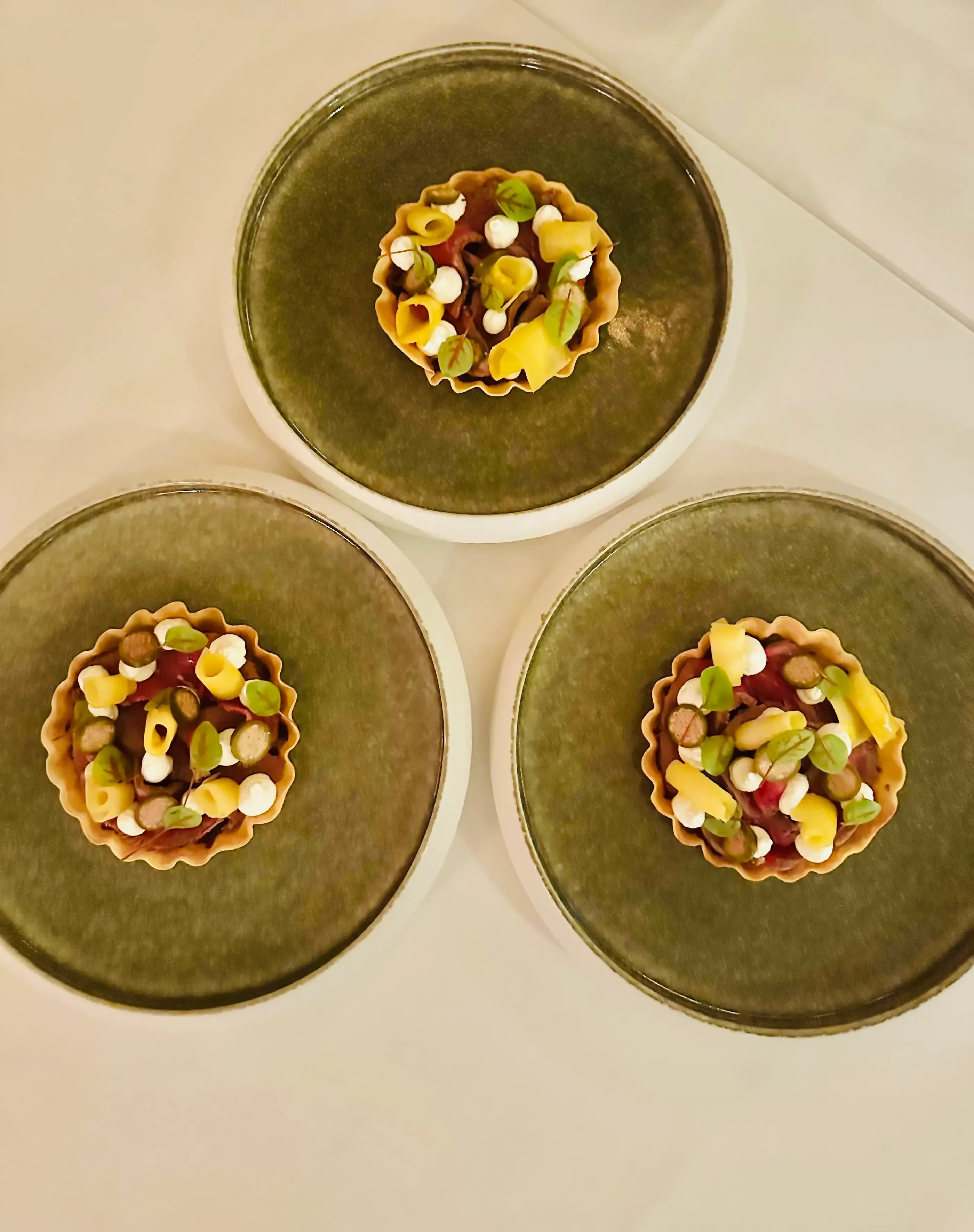 Three small tarts topped with various ingredients on dark green plates