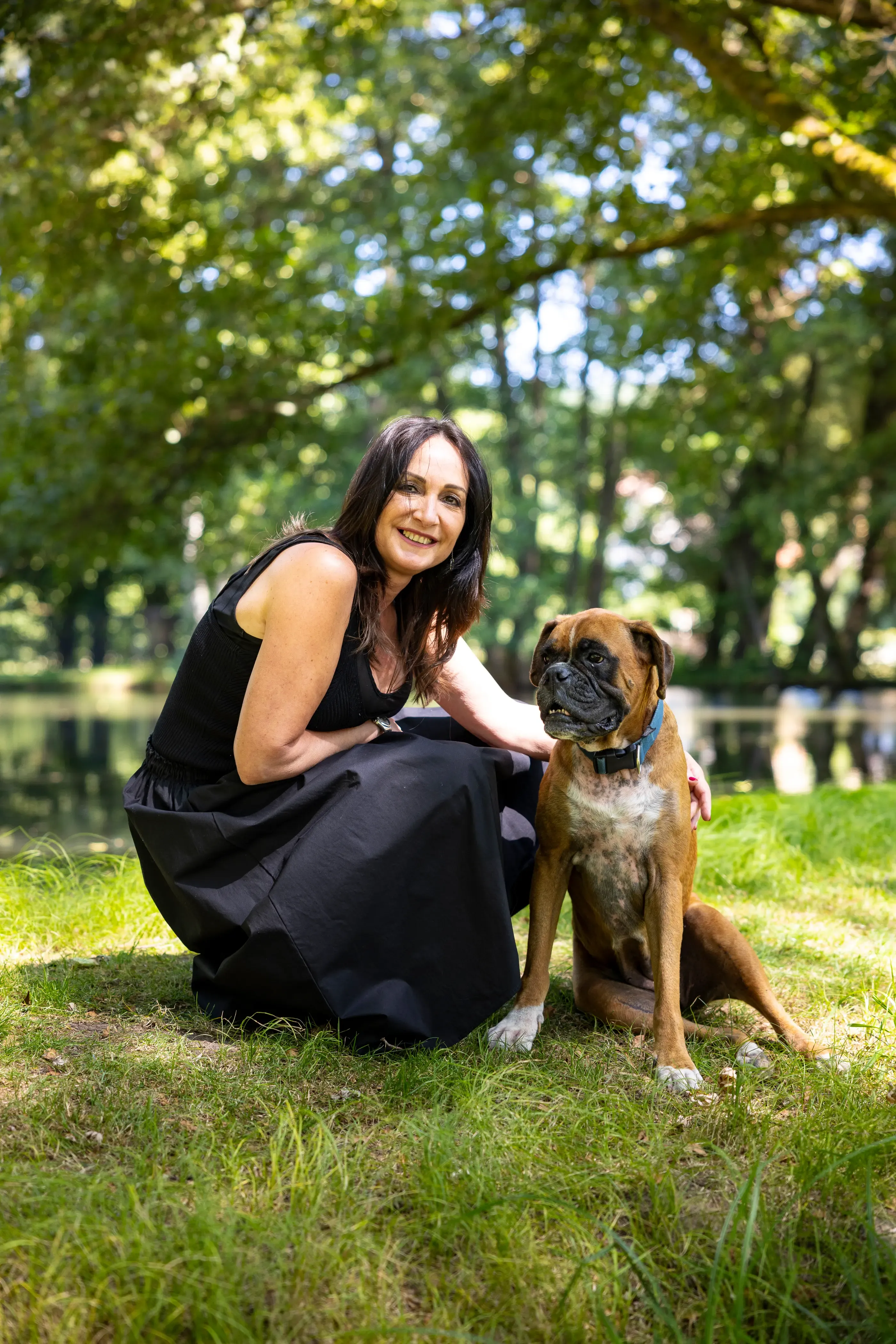 Femme en robe noire accroupie dans un parc avec un chien boxer à côté d'elle