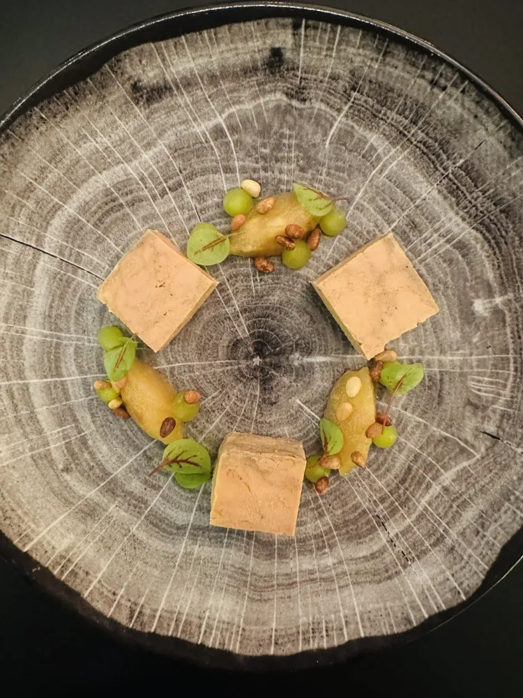 Four pieces of terrine surrounded by fruit and nuts on a metal plate
