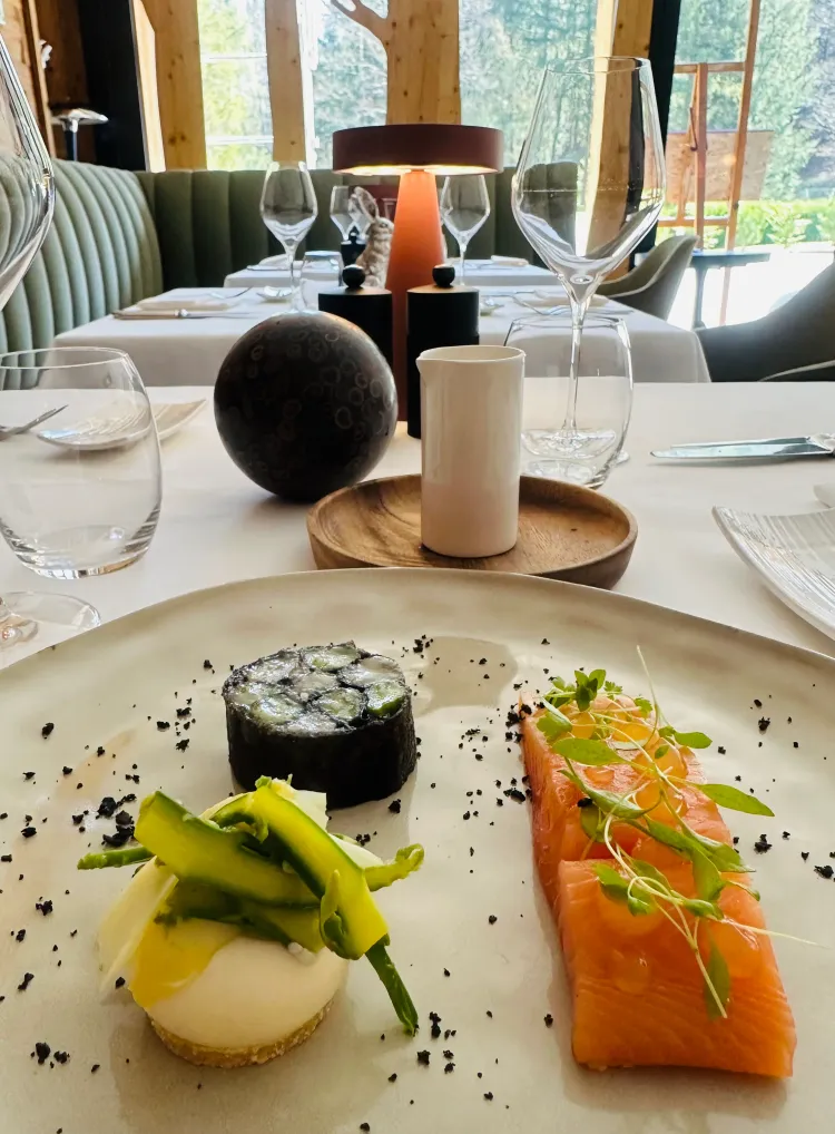 Plate of fine dishes with sushi, salmon, and vegetables, placed on an elegant table with wine glasses and decoration.