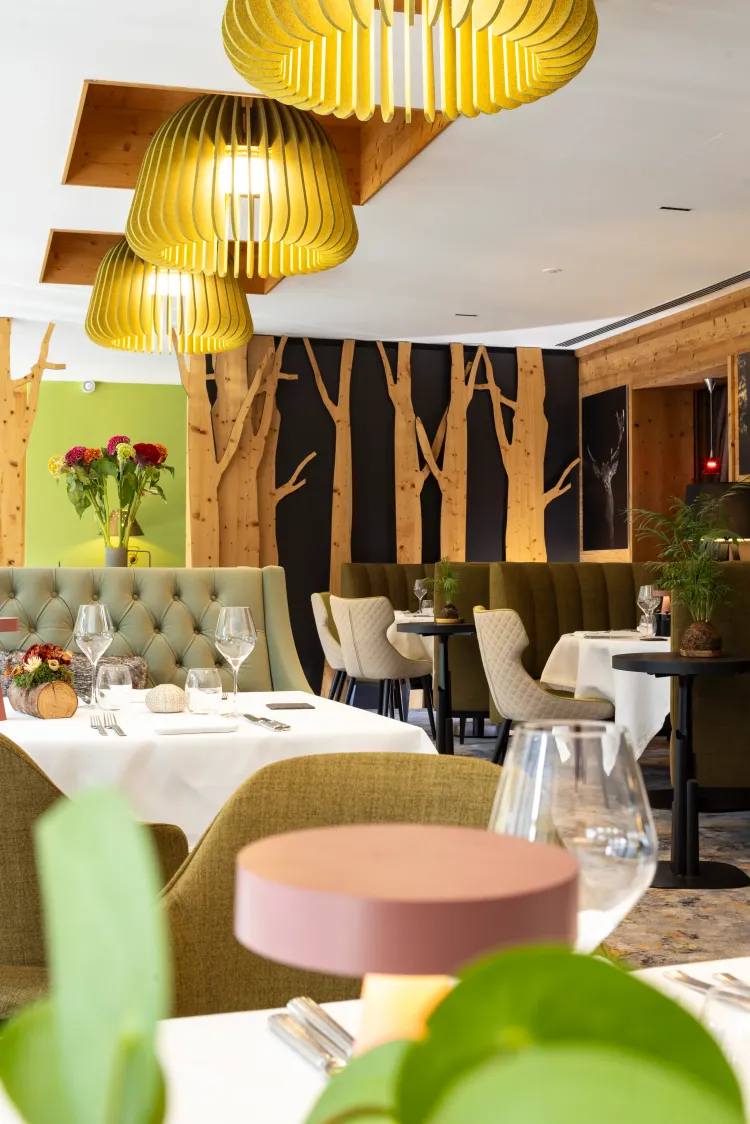 Eleganter Restaurant mit gedeckten Tischen, grünen Sitzbänken und goldenen Pendelleuchten, Holzwänden und dekorativen Pflanzen