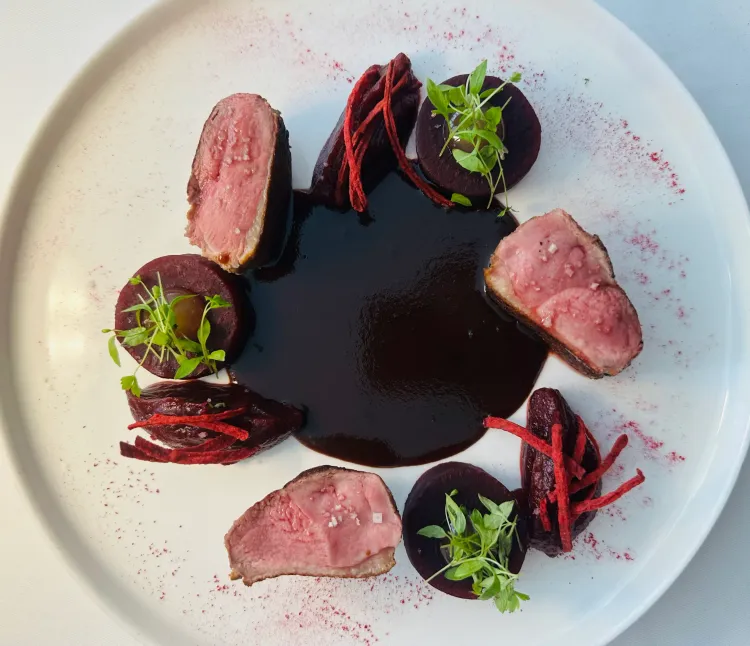Plate with slices of meat, beetroot rounds topped with microgreens, and a sauce in the center.