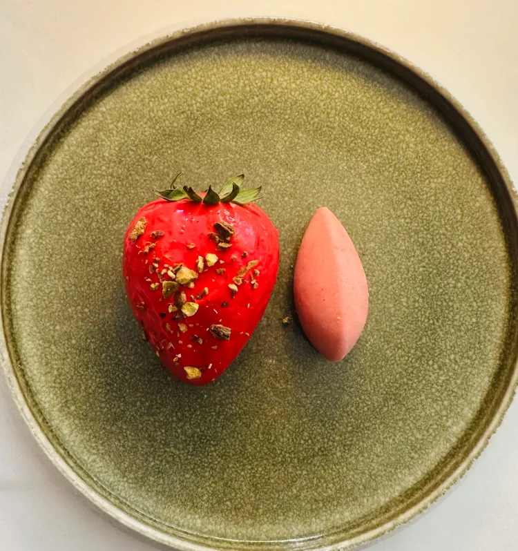 A decorated strawberry and an elongated pink object on a green plate